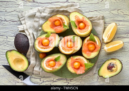 Avocado Boote mit geräuchertem Lachs, Zitrone, Physalis und Minzeblatt, Ansicht von oben an der strukturierten Hintergrund Stockfoto