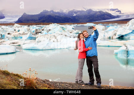 Island - Paar unter selfie self portrait Foto von Gletschersee Jökulsárlón Gletscherlagune/Glacier Lake. Gerne Touristen auf Reisen genießen Sie einen wunderschönen isländischen Natur Landschaft mit Vatnajökull im Hintergrund. Stockfoto