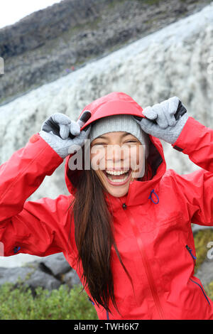 Frau lachend im Regenmantel mit Wasserfall Dettifoss in Island. Aufgeregt Mädchen in Hardshell Besuchen touristischer Attraktionen und Wahrzeichen über Diamond Circle. Wasserfall Dettifoss in Vatnajökull National Park. Stockfoto