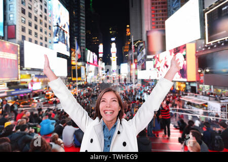 Glücklich, aufgeregt Frau in New York City, Manhattan, Times Square Jubel feiern fröhliche Nachts mit erhobenen Armen. Lächelnd heiteres Multiethnischen asiatischen Kaukasischen Young Urban professional in Ihrem 20s. Stockfoto