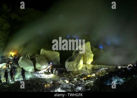 Arbeitnehmer in giftiges Schwefeldioxid Bergbau in Schwefel Bergwerk bei Nacht, Rückseite blau Feuer des Vulkans Ijen, Ijen, Java, Indonesien Stockfoto