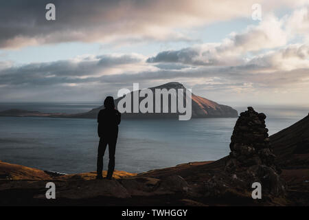 Einsamer Wanderer genießen am Abend Blick auf die Färöer Insel Koltur mit spektakulären Wolken, Sonne, blauer Himmel während des Frühlings (Färöer Inseln) Stockfoto