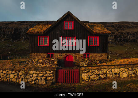 Typische Schwarz und Rot färöischen Holzhaus mit Grasdach als bei Sonnenuntergang im Dorf Kirkjubour im Frühling entdeckt (Färöer Inseln) Stockfoto