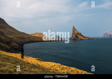 Einsamer Wanderer genießen Panorama Blick Richtung Drangarnir und Tindholmur während am frühen Morgen Wanderung im Frühling (Färöer, Dänemark, Europa) Stockfoto