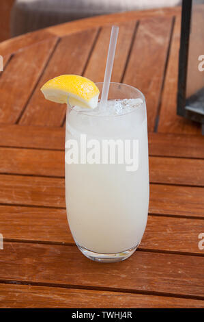 Gekühlte Limonade trinken Trinken mit einer Scheibe Zitrone als Garnitur mit einem klaren Stroh auf einem Holz Picknick Tabelle entnommen. Stockfoto