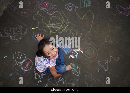 Asiatische Mädchen Zeichnen mit Kreide auf Asphalt. Kreidezeichnungen von einer Filipina Kid. Filipina Mädchen von 7 Jahren spielen mit Kreide. Stockfoto