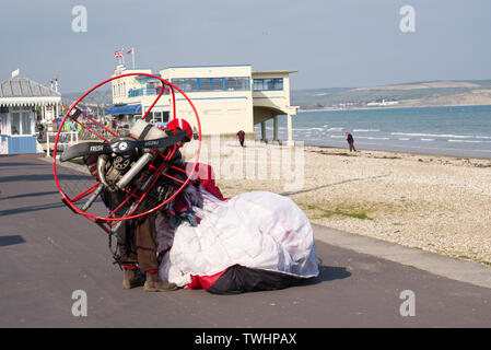 Ein Powered Paragliding Pilot seine Flügel auf dem Weymouth Strandpromenade. Dorchester, Dorset, Großbritannien Stockfoto