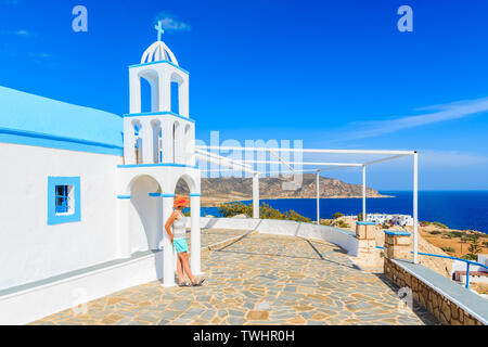 Junge Frau, die Touristen auf der Terrasse des traditionellen weißen Kirche im Dorf Ammopi stehend, Karpathos, Griechenland Stockfoto