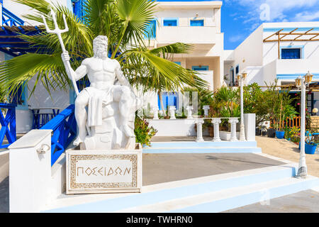 Skulptur von Poseidon, dem Gott des Meeres in der antiken griechischen Religion und Mythos vor typischen Gebäude in Finiki port, Karpathos, Griechenland Stockfoto