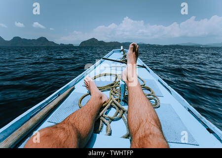 Die Beine des Menschen auf der Banca Boot nähert sich tropische Insel. Reisen, Sommer exotischen Urlaub Urlaub Konzept Stockfoto