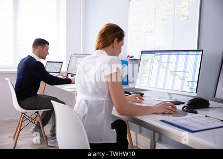 Geschäftsfrau Analyse Gantt-diagramm auf Desktop im Büro zu sitzen hinter männlichen Kollegen Stockfoto