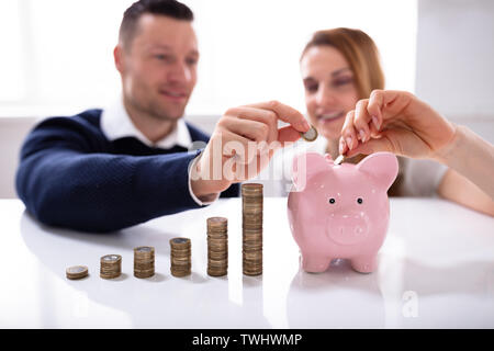 Paar einfügen Münze in Sparschwein in der Nähe von wachsenden Profit über Schreibtisch Stockfoto