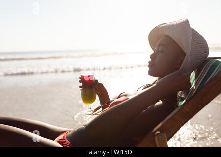 Frau mit Cocktail trinken und entspannen Sie sich in einem Liegestuhl am Strand Stockfoto