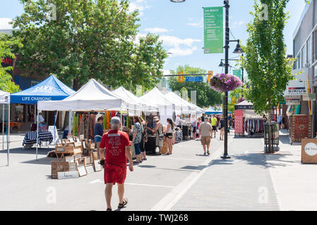 Die Menschen suchen die verschiedenen Tabellen von Waren zum Verkauf an den wöchentlichen Penticton Gemeinschaftsmarkt auf der Main Street Stockfoto