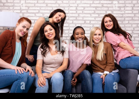 Porträt der Schönen lächelnden Frauen sitzen auf einem Sofa gegen Mauer Stockfoto
