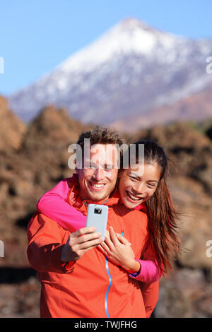 Selfie paar Wandern in schöner Natur mit Smartphone. Glückliches Paar zu Fuß genießen Ansehen und Aufnehmen von Bildern mit der Smart Phone. Mann und Frau, die von Vulkan Teide auf Teneriffa, Kanarische Inseln. Stockfoto