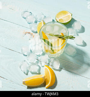 Ein Getränk von Zitrone und Limette in ein elegantes Glas auf einem blauen Hintergrund mit strahlendem Sonnenschein. Sommer Cocktail oder Mojito. Stockfoto