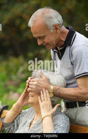 Alter Mann von hinten Womans Augen bedecken und lächelnd Stockfoto