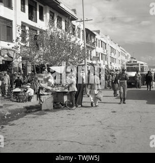1950er Jahre, historische Bild aus dieser Ära, Anzeigen bustingly Aktivität in einer Straße oder Durchgangsstraße in Kabul, Afghanistan, mit Marktständen, Menschen, shopers, Bus und afghanischen Polizisten. Stockfoto