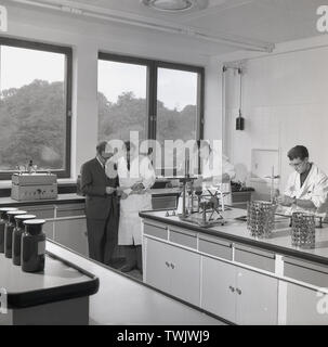1950er Jahre, historische Bild zeigt zwei Krippen und zwei junge männliche Wissenschaftler bei der Arbeit in einem hellen, modernen, Zweck Labor an der Sandoz Chemical Company in Horsforth, Leeds, England, Großbritannien gebaut. Die Firma, die Farbstoffe für den Einsatz in der Textil- und Papierindustrie. Stockfoto