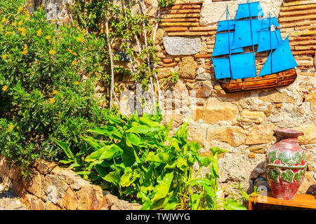 TOSSA DE MAR, SPANIEN - Jun 3, 2019: Shop Display an der Wand mit touristischen Souvenirs in engen Straße mit Häusern aus Stein in der Altstadt von Tossa de Mar, Costa B Stockfoto