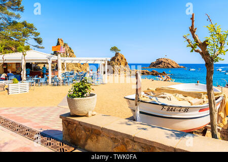 TOSSA DE MAR, SPANIEN - Jun 3, 2019: Fischerboot und Restaurant am Sandstrand in Tossa de Mar, Costa Brava, Spanien. Stockfoto