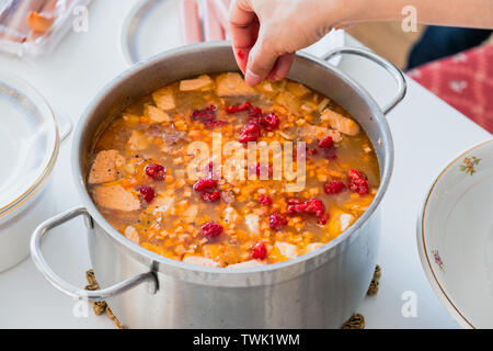 Hand gießen Himbeere in Lachs Suppe mit Karotten und Gemüse in Edelstahl Topf traditionelles Essen Stockfoto