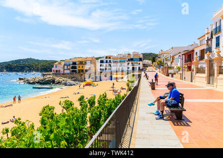 CALELLA DE PALAFRUGELL, SPANIEN - Jul 6, 2019: Paar Touristen sitzen am Strand an der Strandpromenade in der Nähe von canadell Strand von Calella de Palafrugell vi. Stockfoto