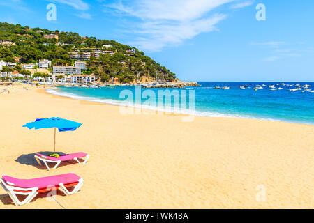 Sonnenliegen mit Sonnenschirm am Sandstrand in Llafranc Dorf, Costa Brava, Spanien Stockfoto