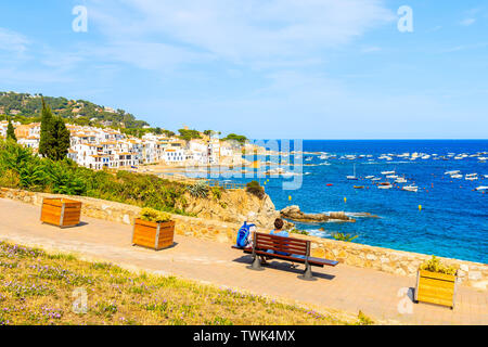 Paar Touristen sitzen auf der Uferpromenade in Calella de Palafrugell, malerischen Fischerdorf mit kleinen Schloss und sandigen Strand mit klarem, blauen wa Stockfoto