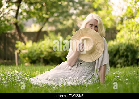 Ältere Frau in Kleid sitzt auf Gras im Park Stockfoto