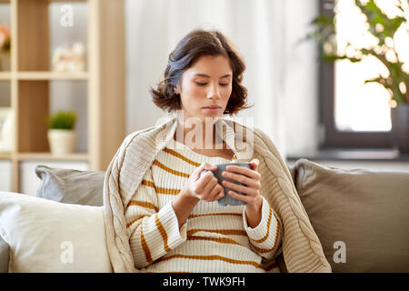 Traurig kranke junge Frau trinkt heißen Tee zu Hause. Stockfoto