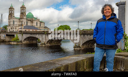 Wunderschöne reife Mexikanischen lächelnde Frau mit blauen Jacke mit der Brücke über den Fluss Shannon in den Hintergrund in der Stadt Athlone Stockfoto