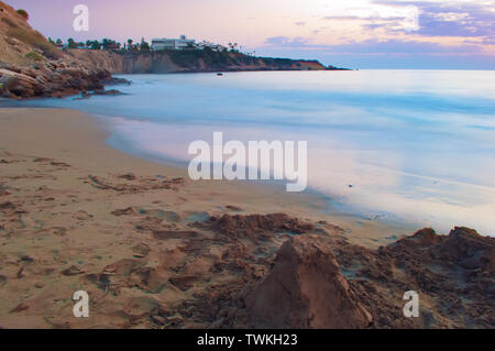 Anzeigen von leeren Sandstrand Coral Bay Beach in der Nähe von Paphos, raucherregelung. Sonnenuntergang, rosa Himmel über hellblau Flachwasser, Villen auf der Klippe. Warmen Abend im Herbst. C Stockfoto