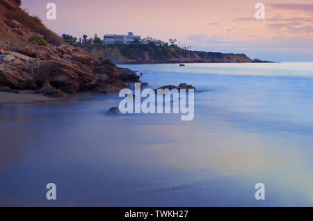 Anzeigen von leeren Sandstrand Coral Bay Beach in der Nähe von Paphos, raucherregelung. Sonnenuntergang, rosa Himmel über hellblau Flachwasser, Villen auf der Klippe. Warmen Abend im Herbst. C Stockfoto