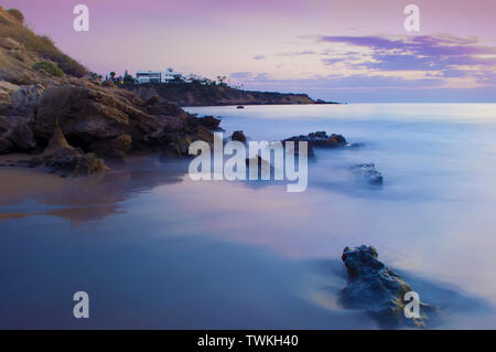 Anzeigen von leeren Sandstrand Coral Bay Beach in der Nähe von Paphos, raucherregelung. Sonnenuntergang, rosa Himmel über hellblau Flachwasser, Villen auf der Klippe. Warmen Abend im Herbst. C Stockfoto