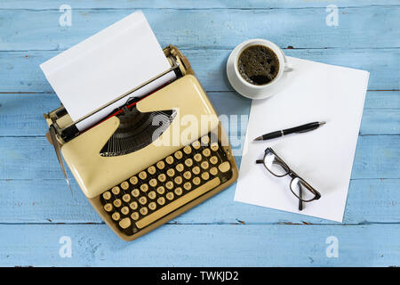 Alte beige Schreibmaschine aus den 50er Jahren mit Papier, Kaffee und Gläser auf ein blau lackierten Holz-, Winkel, Ansicht von oben Stockfoto