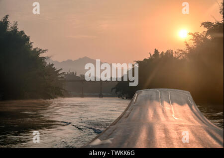 Segeln Long-tail-Boot mit Sonnenaufgang auf der Brücke in den Fluss Kwai in Kanchanaburi Stockfoto