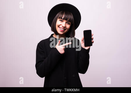 Glücklich verlassen brunette Mädchen in schwarzen Hut zeigt mit dem Finger auf leere mobile Leinwand, auf grauem Hintergrund Stockfoto