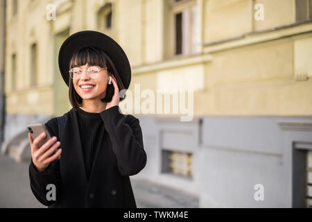 Glückliche Frau mit Kopfhörer auf das Mobiltelefon in der Stadt Stockfoto