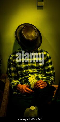 Männchen in einem Flanellhemd und einem Cowboyhut schlafend Beim Sitzen in der Nähe einer Wand Stockfoto