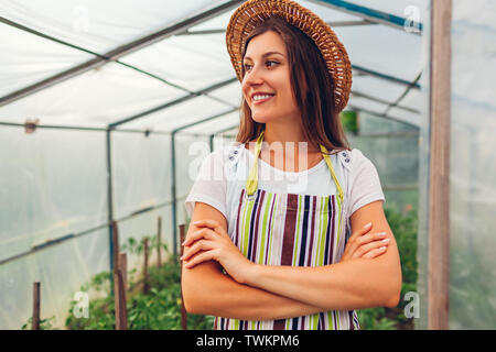 Frau Bauer im Gewächshaus. Glückliche Arbeiter Anbau von Gemüse und Stolz auf ihre Arbeit im Treibhaus. Agrar- und Landwirtschaft Konzept. Organic Farm Stockfoto