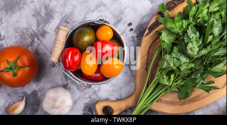 Grüne Petersilie auf einem Holzbrett neben Cherry Tomaten und Knoblauch, Salz und Pfeffer auf einem grauen Tabelle. Zutaten zum Kochen. Ansicht von oben, l Stockfoto