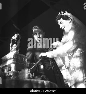 Kirchliche Trauung c 1946 Name der Maurer - Schneiden Sie den Kuchen mit ein zeremonielles Schwert bei natürlichem Licht mit Schatten aus einem Fenster Foto von Gilbert Gilbert Adams Adams aus der Sammlung vollständig im Besitz von Tony Henshaw Stockfoto