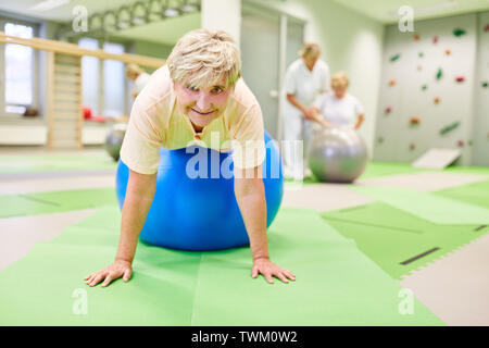 Ältere Frau tut Übung auf der übung Kugel für die Ausbildung in der Physiotherapie Stockfoto