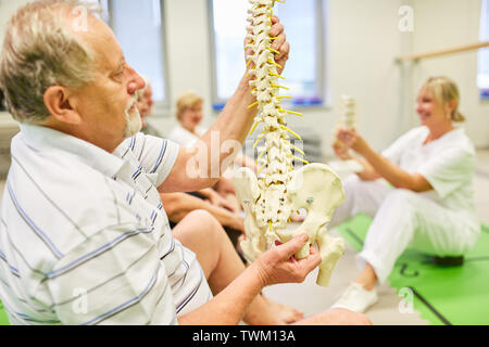 Senior hält Wirbelsäule Modell in einer Rückenschule oder Rehabilitation Rückentraining Stockfoto