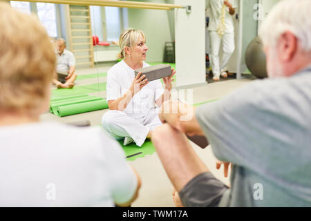 Trainer mit Yoga block erklärt Senioren gesund zurück Übung in der Physiotherapie Klasse Stockfoto