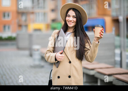 Hübsche junge business Frau mit einer Tasse Kaffee und Dateien gehen auf die Straße Stockfoto