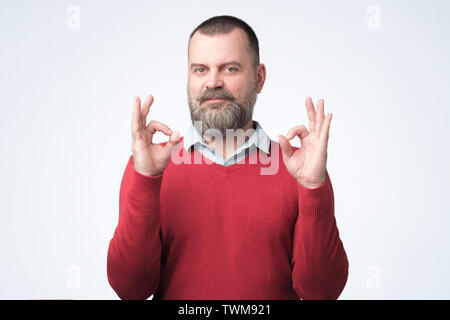 Reifer Mann im roten Pullover mit OK Zeichen Stockfoto