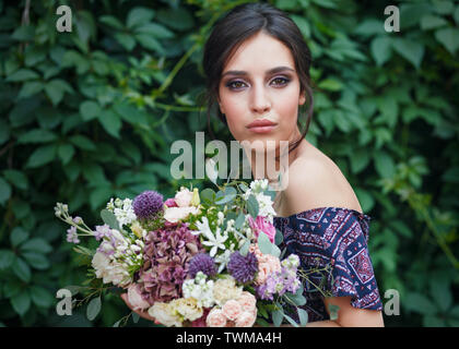 Porträt einer wunderschönen jungen Frau mit perfektem Make-up und Frisur, während Sie einen Strauß Wildblumen. Der Efeu an der Wand. Die CONCE Stockfoto